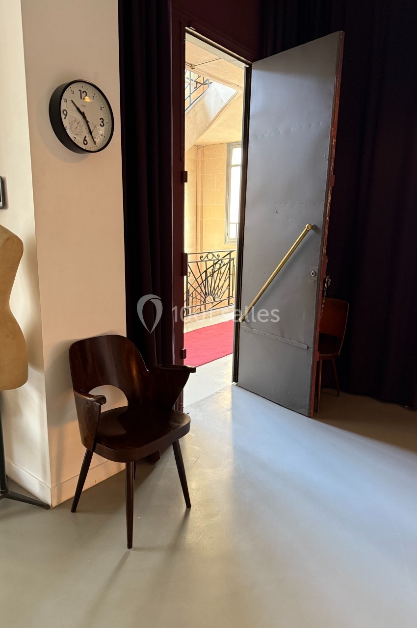 Location salle Paris 20 (Paris) - Studio 7 #49 Une chaise en bois et un mannequin près d'une porte ouverte donnant sur un couloir lumineux avec une rambarde en fer forgé.