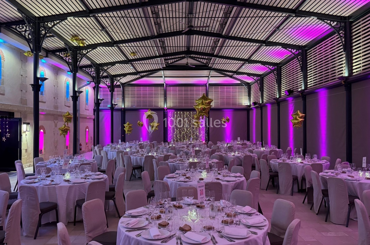 Salle de réception décorée avec des tables rondes dressées, éclairage violet et doré, et ballons en forme d'étoiles.