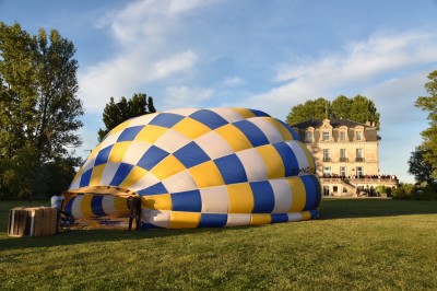 Montgolfière en cours de gonflage sur une pelouse, avec un manoir en arrière-plan et des arbres environnants.