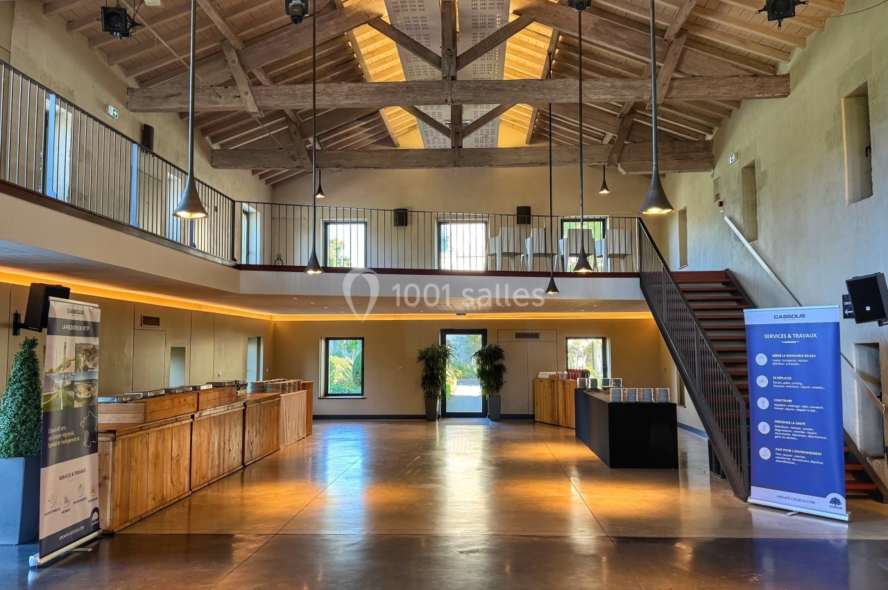 Salle lumineuse avec charpente en bois apparente, mezzanine, escalier, et présentoirs en bois sur un sol en béton poli.