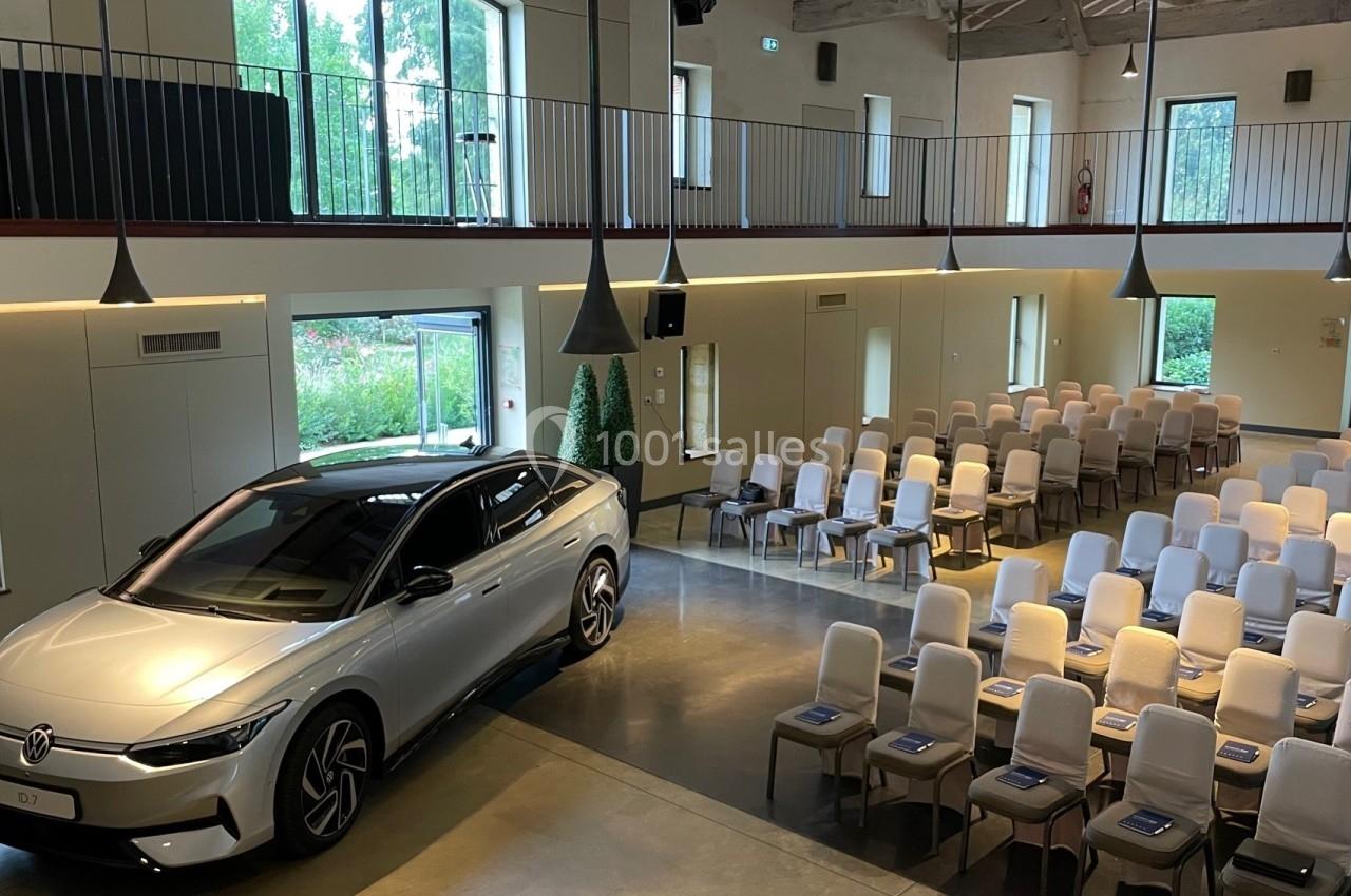 Voiture argentée exposée dans une salle lumineuse avec des rangées de chaises disposées pour un événement.