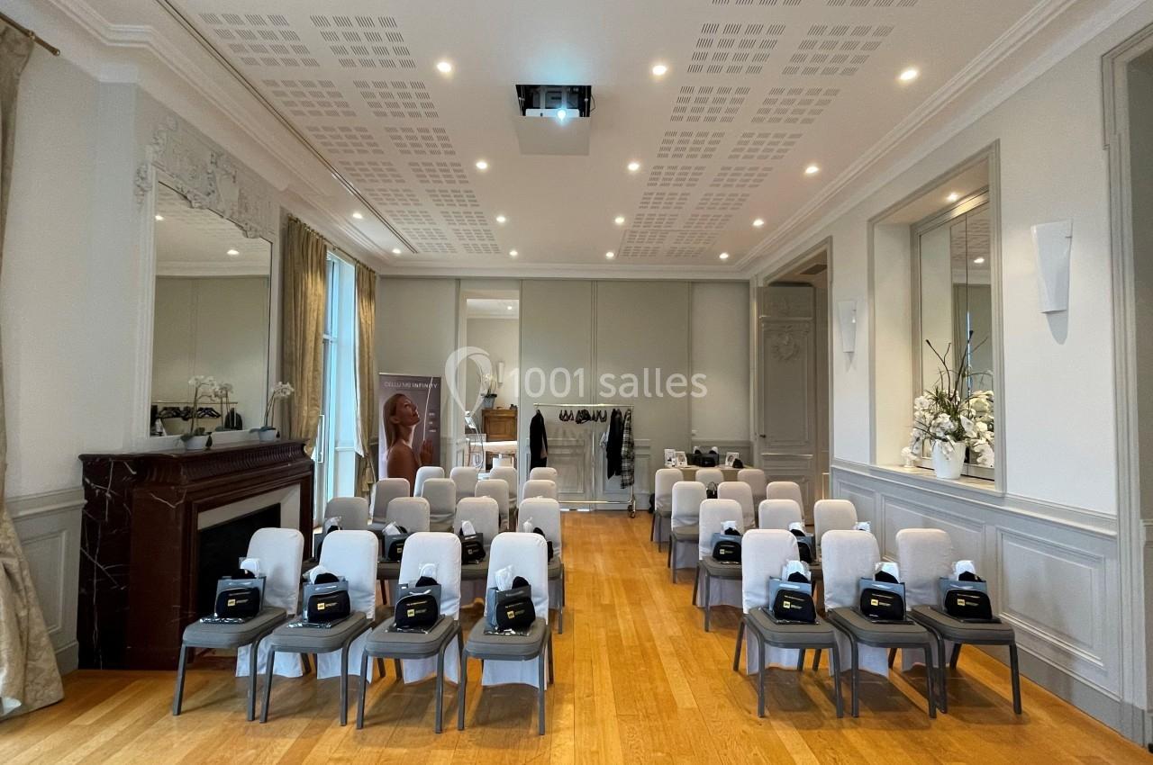 Salle de conférence lumineuse avec des rangées de chaises alignées, équipées de sacs noirs, et un écran de projection au…