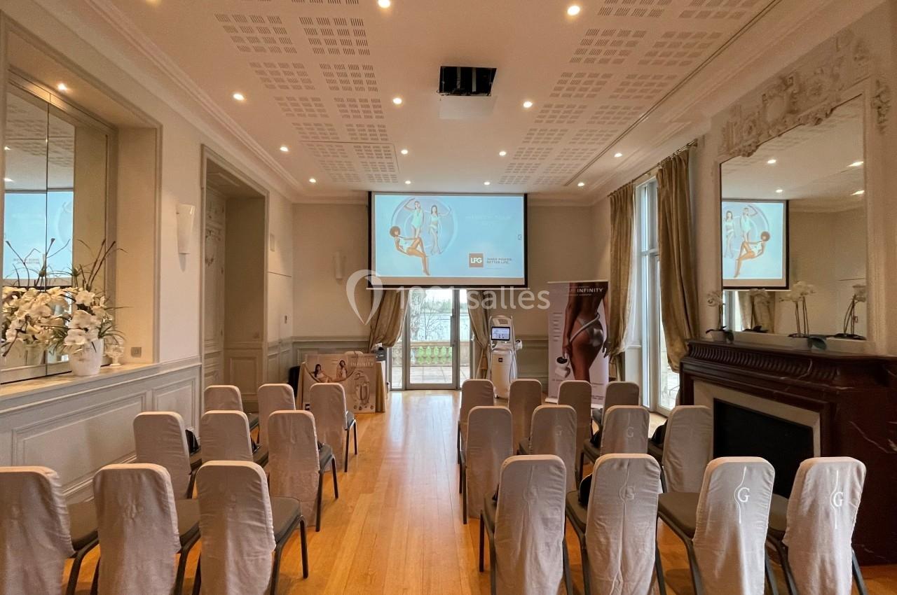 Salle de conférence lumineuse avec chaises alignées, écran de projection allumé et décorations élégantes.