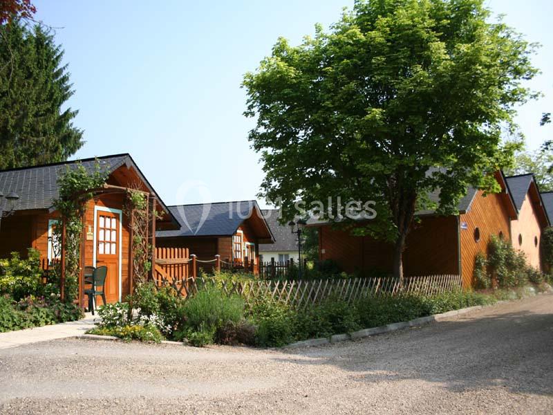 Alignement de chalets en bois entourés de végétation, avec un arbre central et une allée en gravier au premier plan.