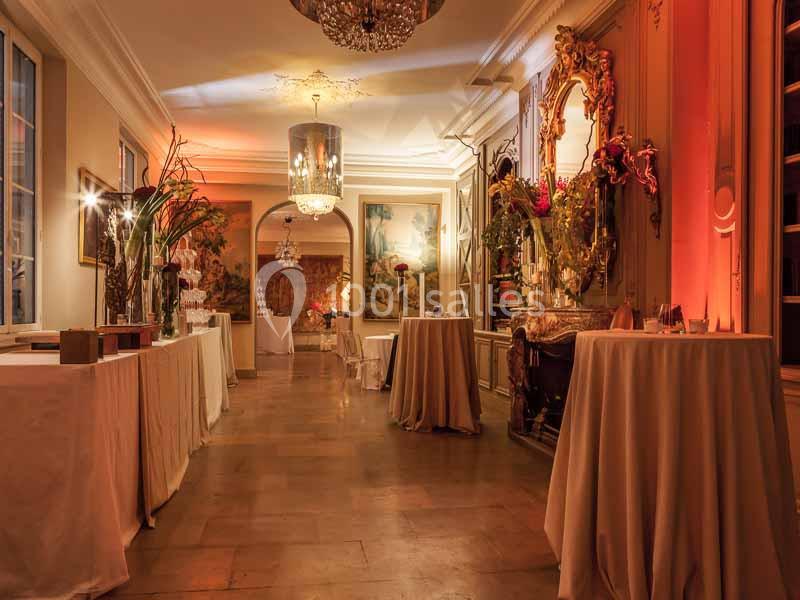 Salle élégante avec tables drapées, décorations florales, miroirs dorés et éclairage chaleureux.