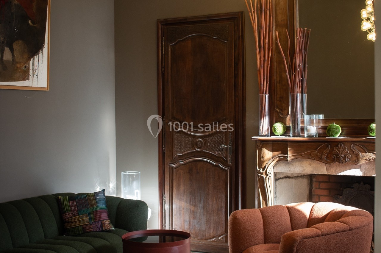 Salon élégant avec fauteuils colorés, table basse ronde, cheminée ornée et suspension lumineuse moderne.