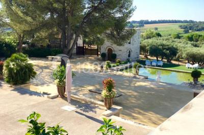 Tour en pierre entourée de végétation, avec bassin d'eau, chaises et tables en métal sur une terrasse ensoleillée.