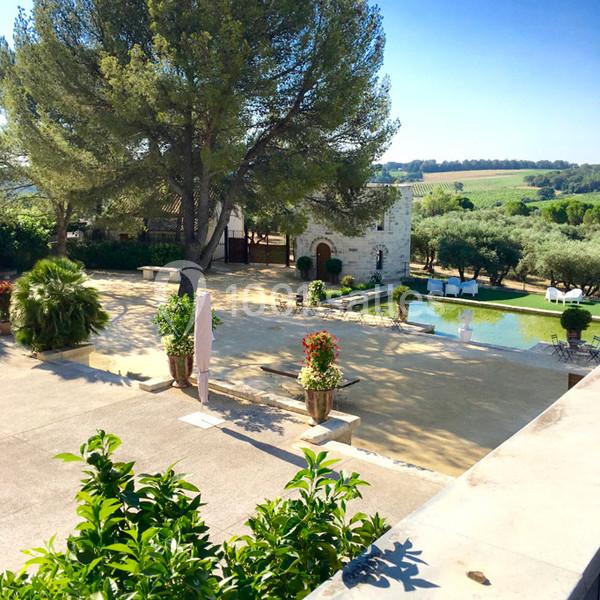 Cour extérieure avec piscine, arbres, plantes en pot et bâtiment en pierre, entourée de champs et d'arbres.