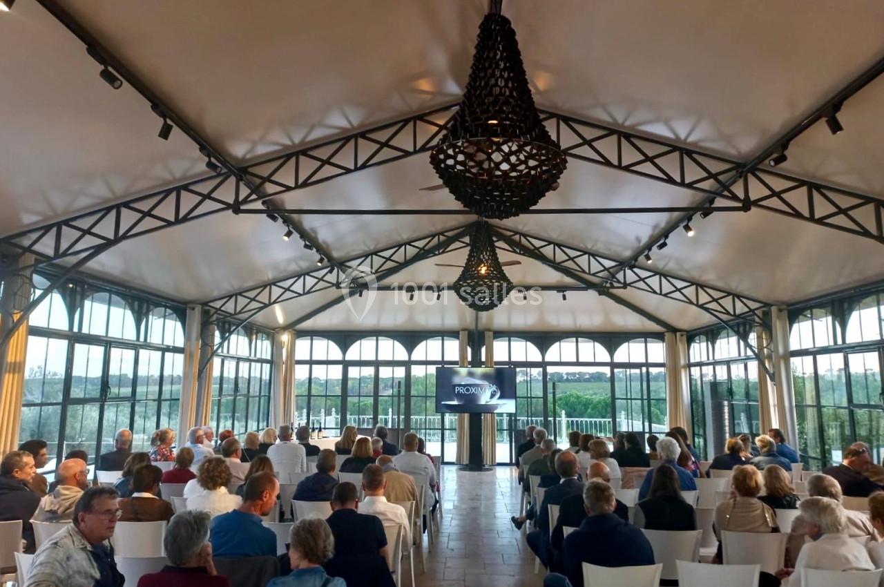 Salle lumineuse avec des invités assis, regardant une présentation sur un écran sous une structure en métal et toile.