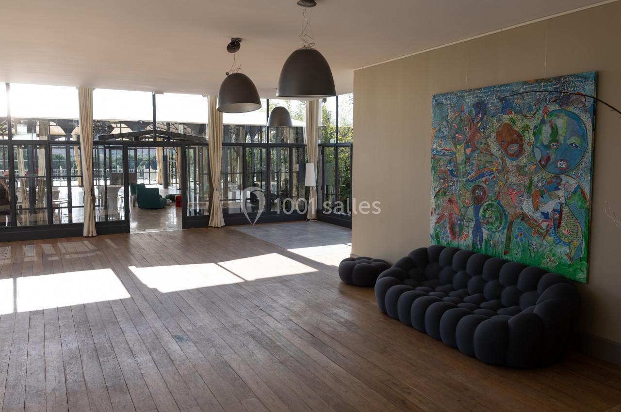 Salle lumineuse avec parquet, canapé moderne, tableau coloré au mur et grandes baies vitrées donnant sur une terrasse.