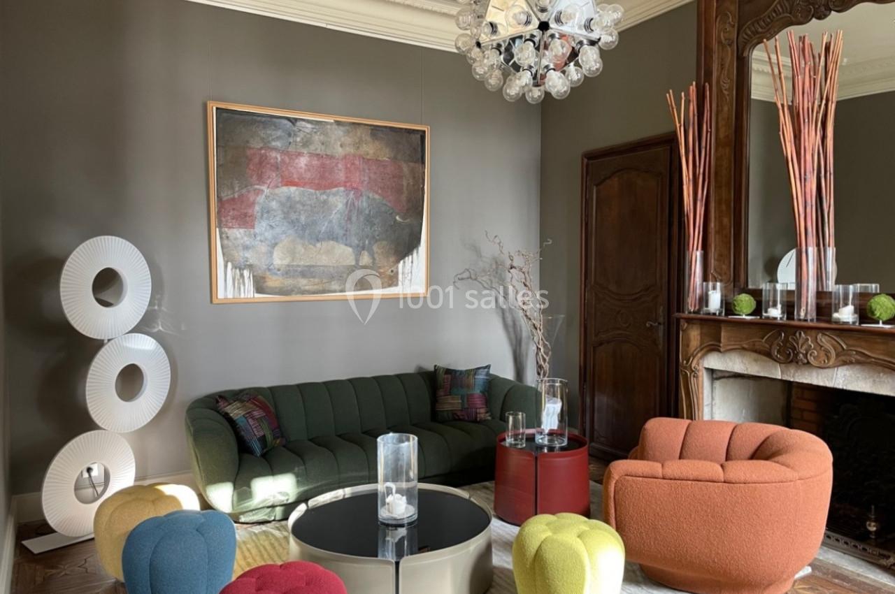 Salon élégant avec canapé vert, fauteuil orange, table basse, cheminée ornée et décoration moderne colorée.