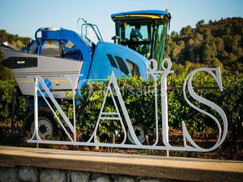 Machine agricole bleue dans un vignoble avec une structure métallique affichant le mot ’NAÏS’ au premier plan.