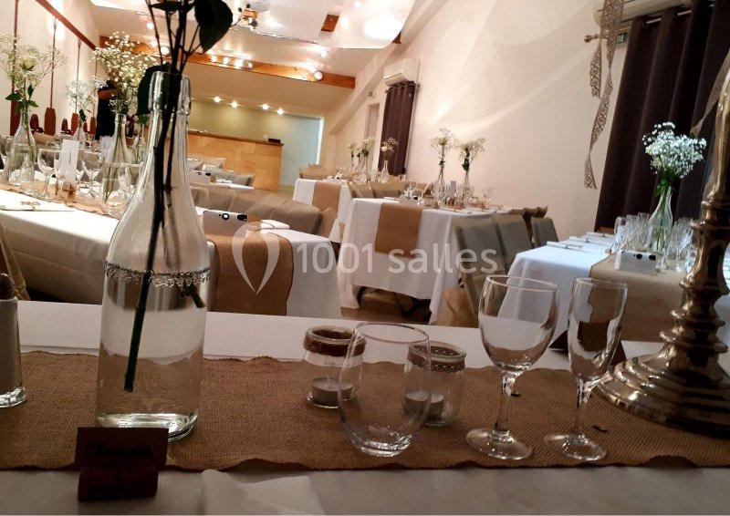 Salle de réception décorée avec des tables dressées, nappes blanches, chemins de table en jute et bouquets de fleurs.