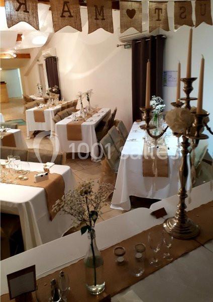 Salle de réception décorée pour un mariage avec nappes blanches, chemins de table en jute et chandeliers dorés.