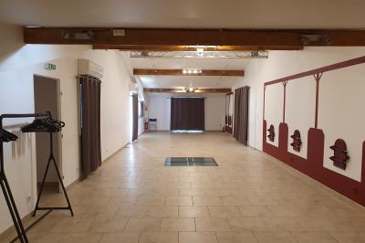 Salle lumineuse avec murs blancs et rouges, sol en carrelage beige, poutres apparentes et comptoir en pierre au fond.