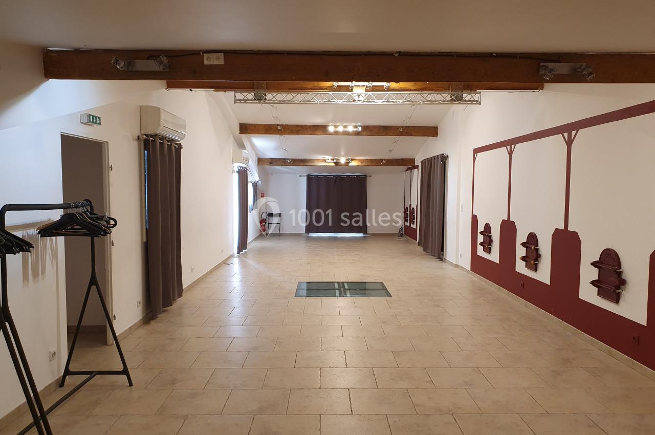 Salle vide avec carrelage beige, poutres apparentes, murs blancs et rouges, et portants à vêtements sur la gauche.