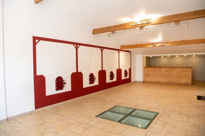 Salle lumineuse avec murs blancs et rouges, sol en carrelage beige, poutres apparentes et comptoir en pierre au fond.