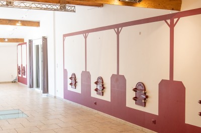 Salle lumineuse avec murs blancs et rouges, sol en carrelage beige, poutres apparentes et comptoir en pierre au fond.