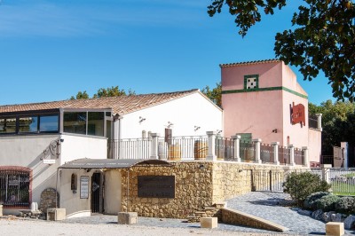 Salle lumineuse avec murs blancs et rouges, sol en carrelage beige, poutres apparentes et comptoir en pierre au fond.