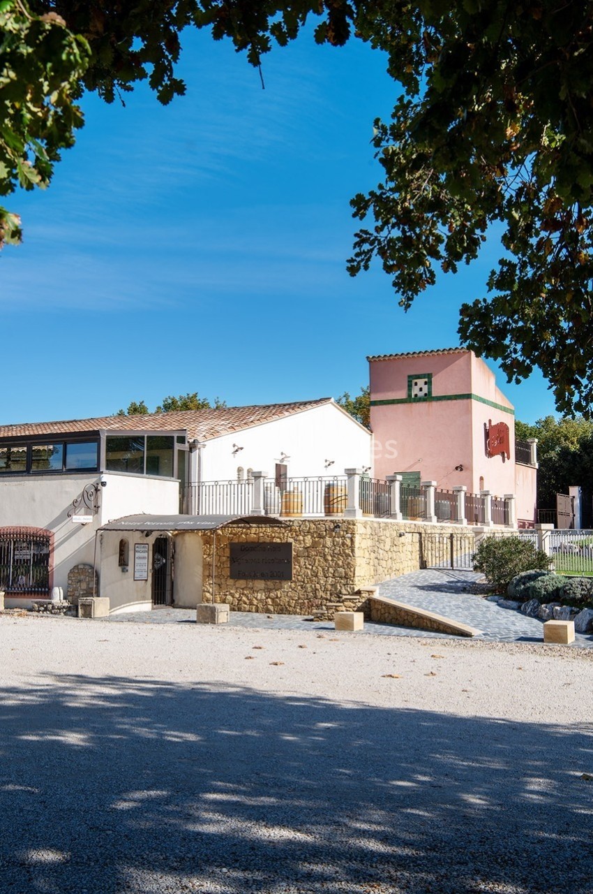 Bâtiment aux façades blanches et roses entouré de végétation, avec un ciel bleu dégagé en arrière-plan.