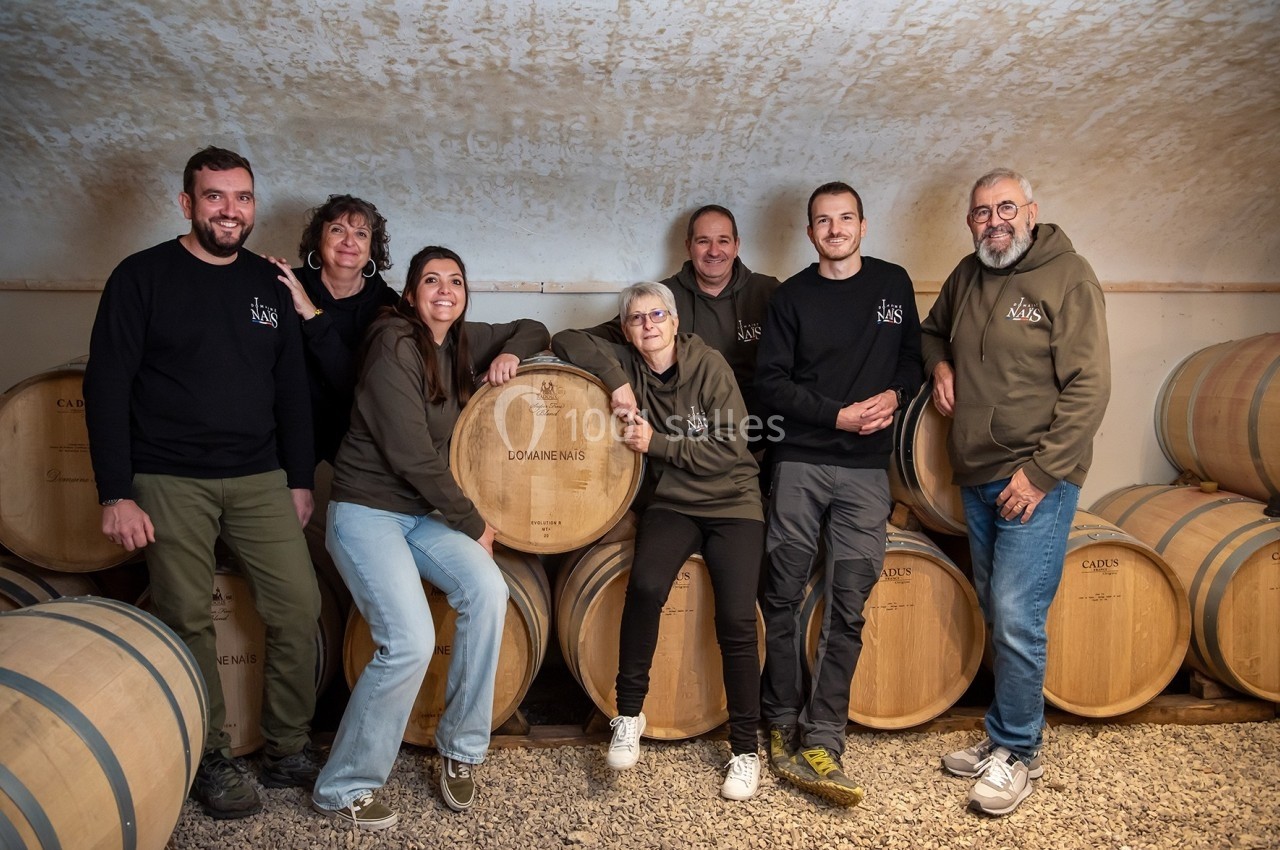 Location salle Rognes (Bouches-du-Rhône) - Domaine Naïs #12 Un groupe de personnes pose devant des fûts en bois dans une cave voûtée.