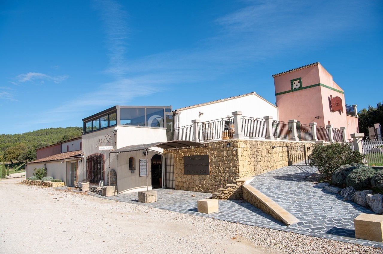 Location salle Rognes (Bouches-du-Rhône) - Domaine Naïs #7 Bâtiment en pierre et crépi avec terrasse, entouré de végétation sous un ciel bleu clair.