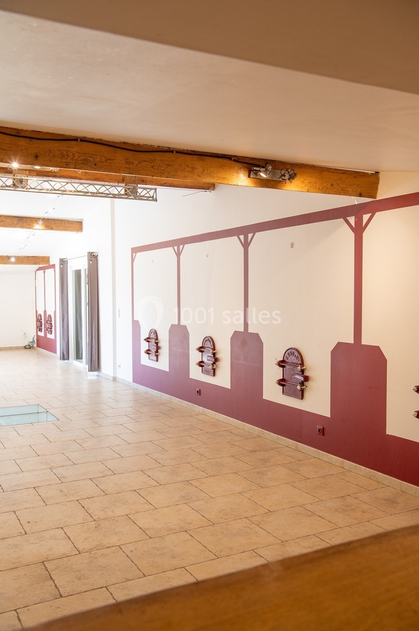 Location salle Rognes (Bouches-du-Rhône) - Domaine Naïs #11 Mur intérieur avec décorations murales rouges, sol en carrelage beige et poutres apparentes au plafond.