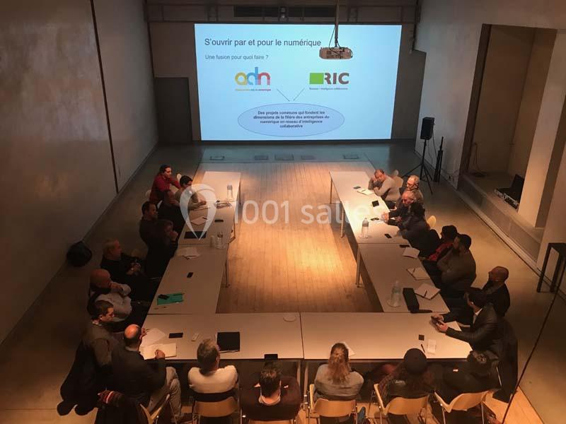 Réunion autour d'une grande table en U, avec des participants et une présentation projetée sur un écran.
