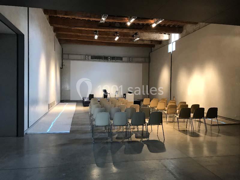 Location salle Avignon (Vaucluse) - Le Grenier à Sel #7 Salle vide avec des rangées de chaises beige et noires, un projecteur et un pupitre devant un mur blanc.