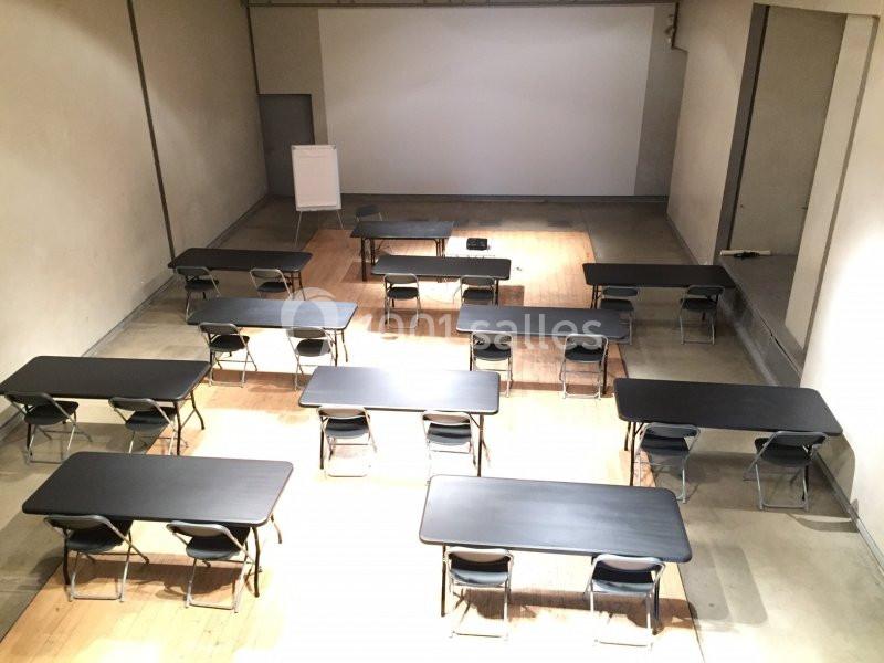 Location salle Avignon (Vaucluse) - Le Grenier à Sel #9 Salle de réunion avec des tables noires alignées, des chaises pliantes et un tableau de présentation au fond.