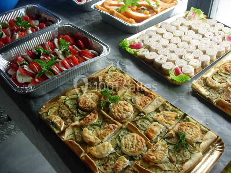 Plateaux de nourriture variée comprenant tartes salées, roulés apéritifs, salade de tomates et melon tranché.