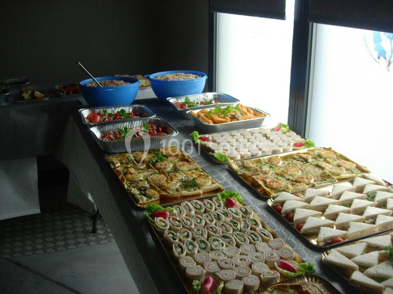 Buffet varié avec sandwichs, roulés, salades et plats disposés sur une table près de fenêtres.