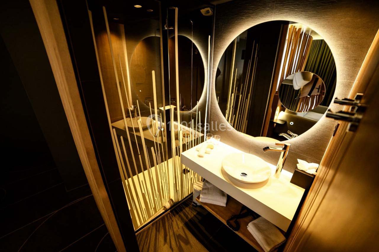 Location salle Montpellier (Hérault) - Hôtel Belaroïa #16 Salle de bain moderne avec lavabo rond, miroir éclairé et paroi de douche ornée de motifs verticaux.