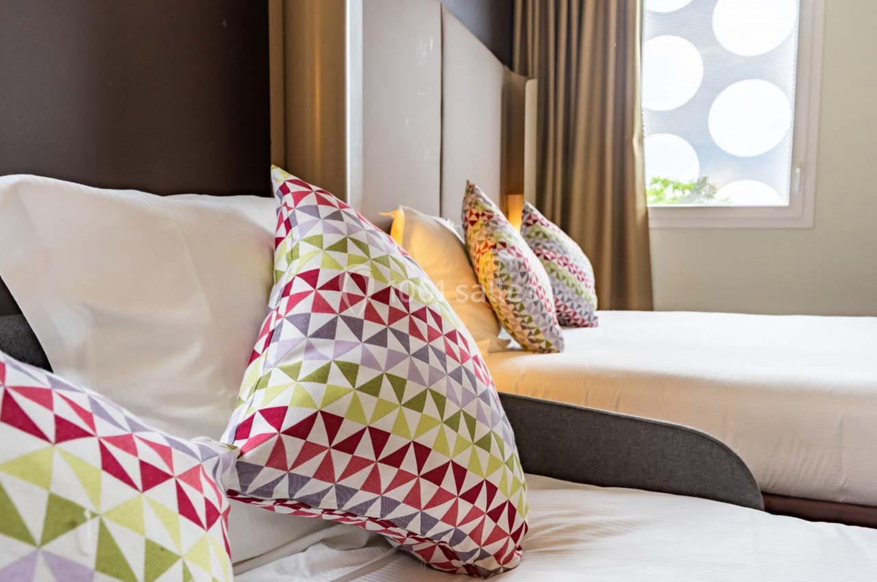 Location salle Montpellier (Hérault) - Hôtel Belaroïa #11 Deux lits avec des coussins colorés à motifs géométriques dans une chambre lumineuse avec un rideau beige.