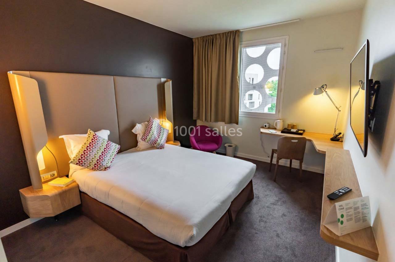 Location salle Montpellier (Hérault) - Hôtel Belaroïa #10 Chambre d'hôtel moderne avec lit double, bureau, fauteuil rose, télévision murale et fenêtre donnant sur l'extérieur.