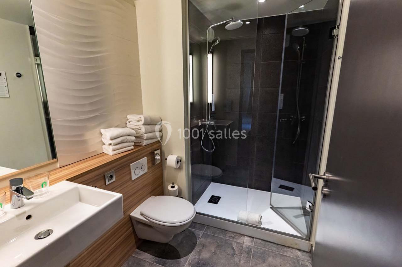 Location salle Montpellier (Hérault) - Hôtel Belaroïa #18 Salle de bain moderne avec douche vitrée, lavabo, toilettes et serviettes pliées sur un plan de travail en bois.