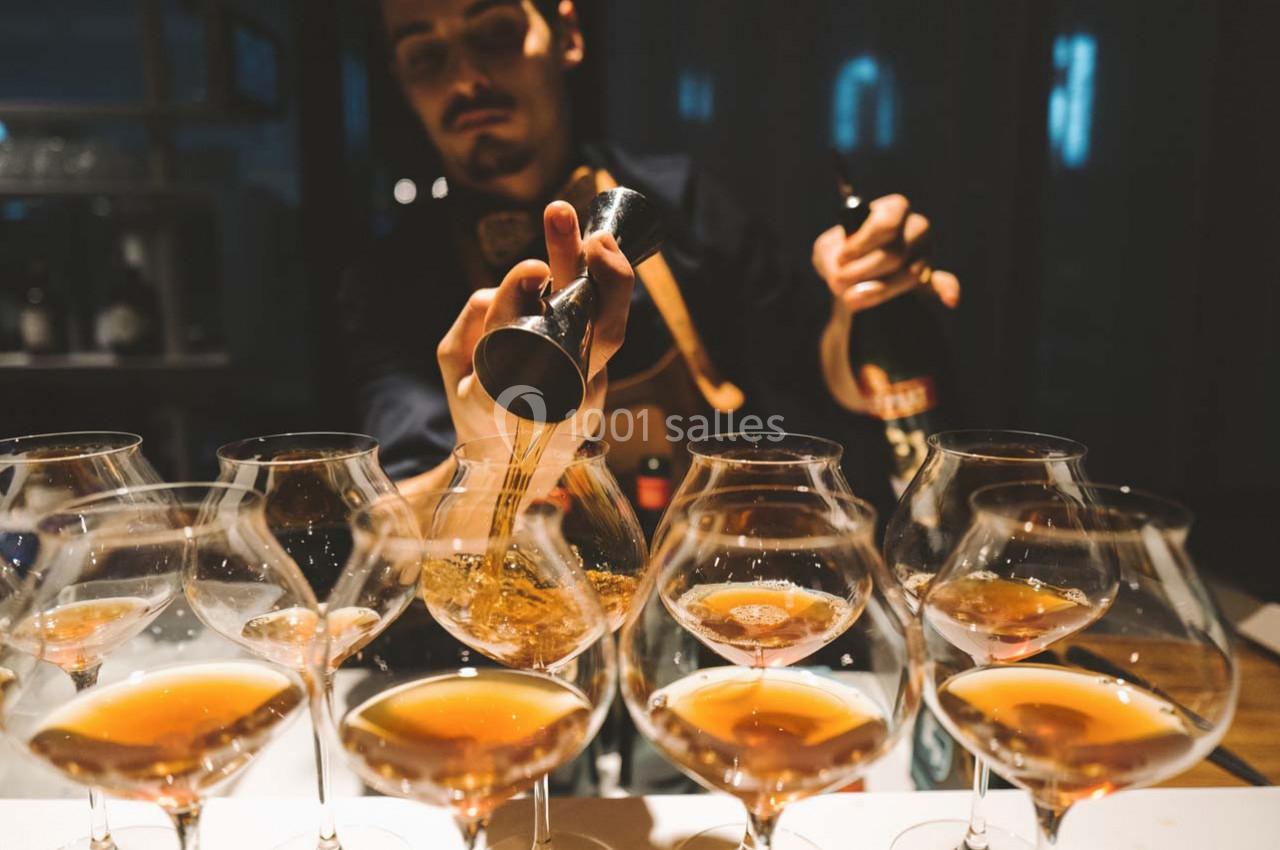 Location salle Montpellier (Hérault) - Hôtel Belaroïa #6 Un barman verse un liquide ambré dans des verres à pied alignés sur un comptoir, dans une ambiance tamisée.