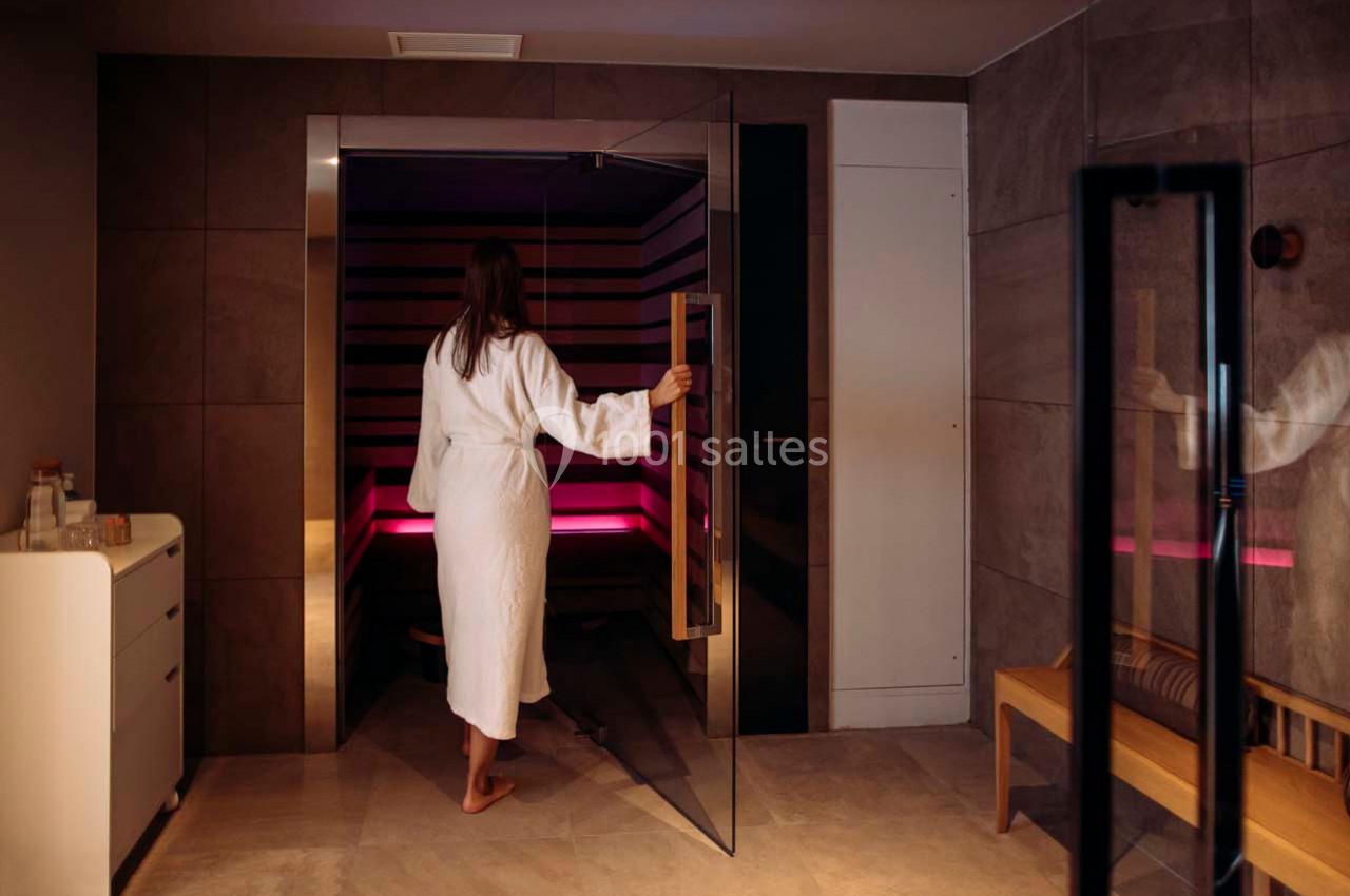 Location salle Montpellier (Hérault) - Hôtel Belaroïa #26 Une femme en peignoir entre dans un sauna moderne aux parois en bois, éclairé par une lumière tamisée.