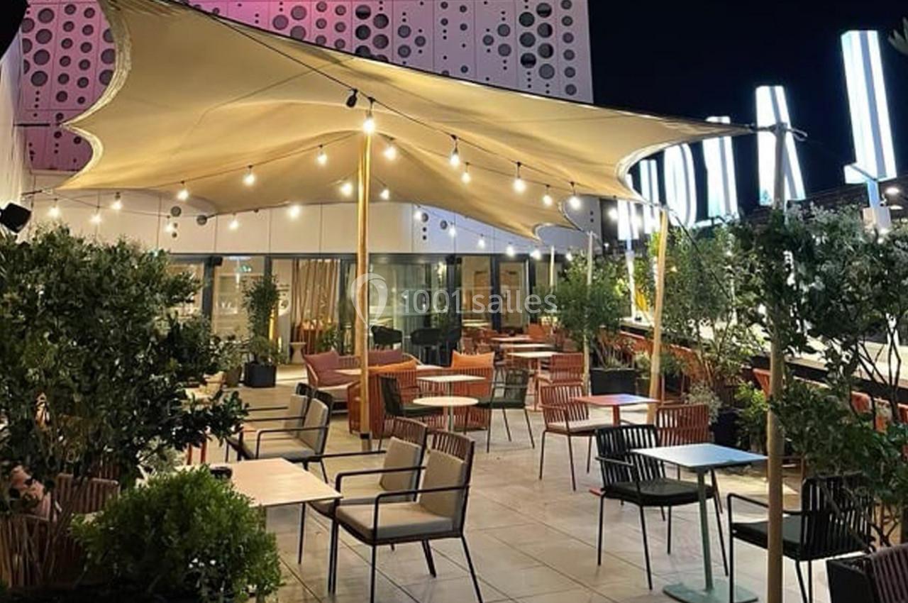 Location salle Montpellier (Hérault) - Hôtel Belaroïa #22 Terrasse extérieure éclairée de nuit avec tables, chaises, plantes et une toile tendue moderne en guise d'abri.