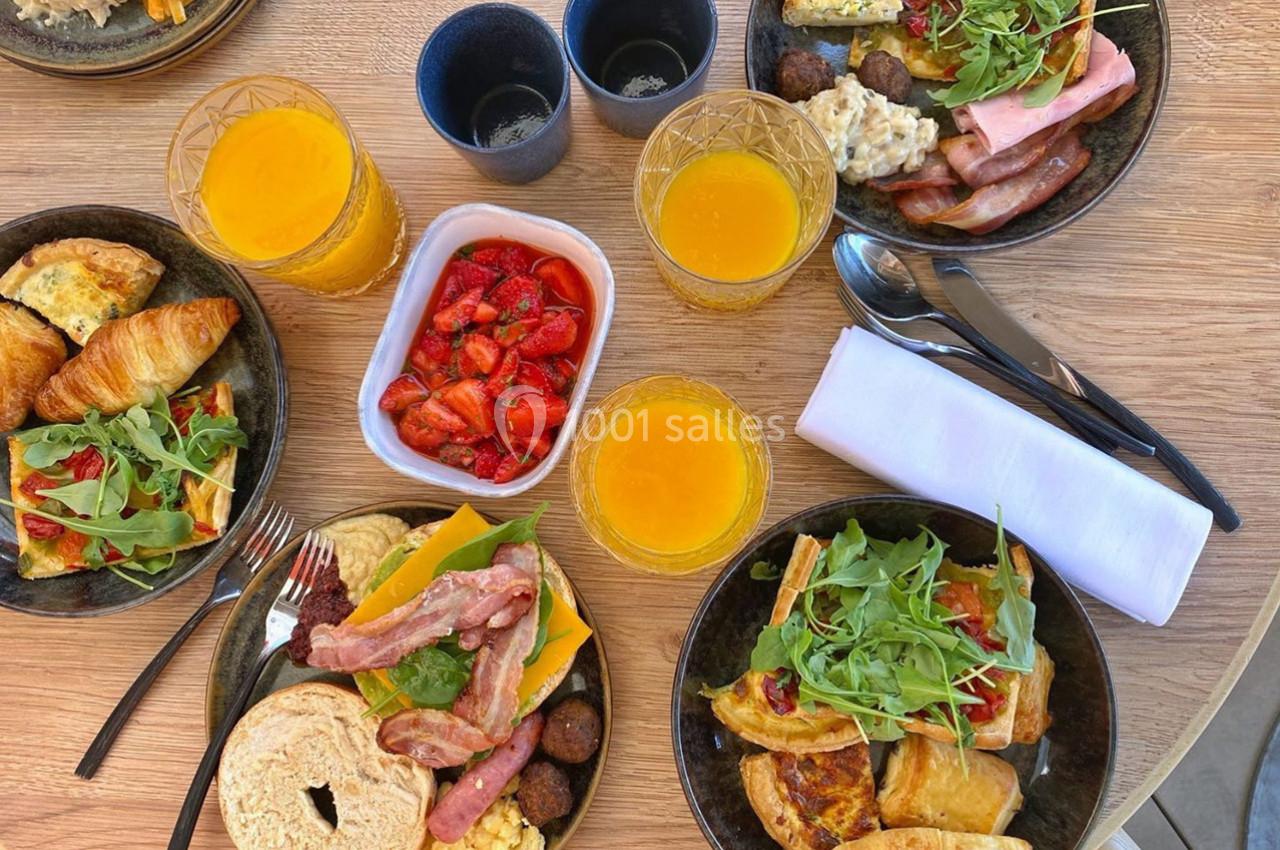Location salle Montpellier (Hérault) - Hôtel Belaroïa #25 Petit-déjeuner varié avec croissants, œufs, bacon, fruits frais, jus d'orange et couverts sur une table en bois.