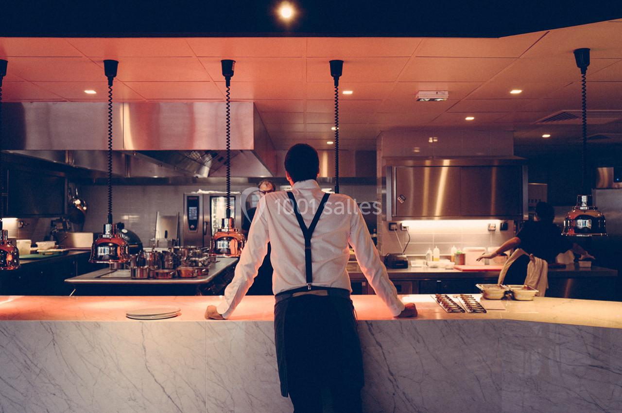 Location salle Montpellier (Hérault) - Hôtel Belaroïa #5 Un serveur en tenue formelle se tient derrière un comptoir en marbre dans une cuisine ouverte éclairée.