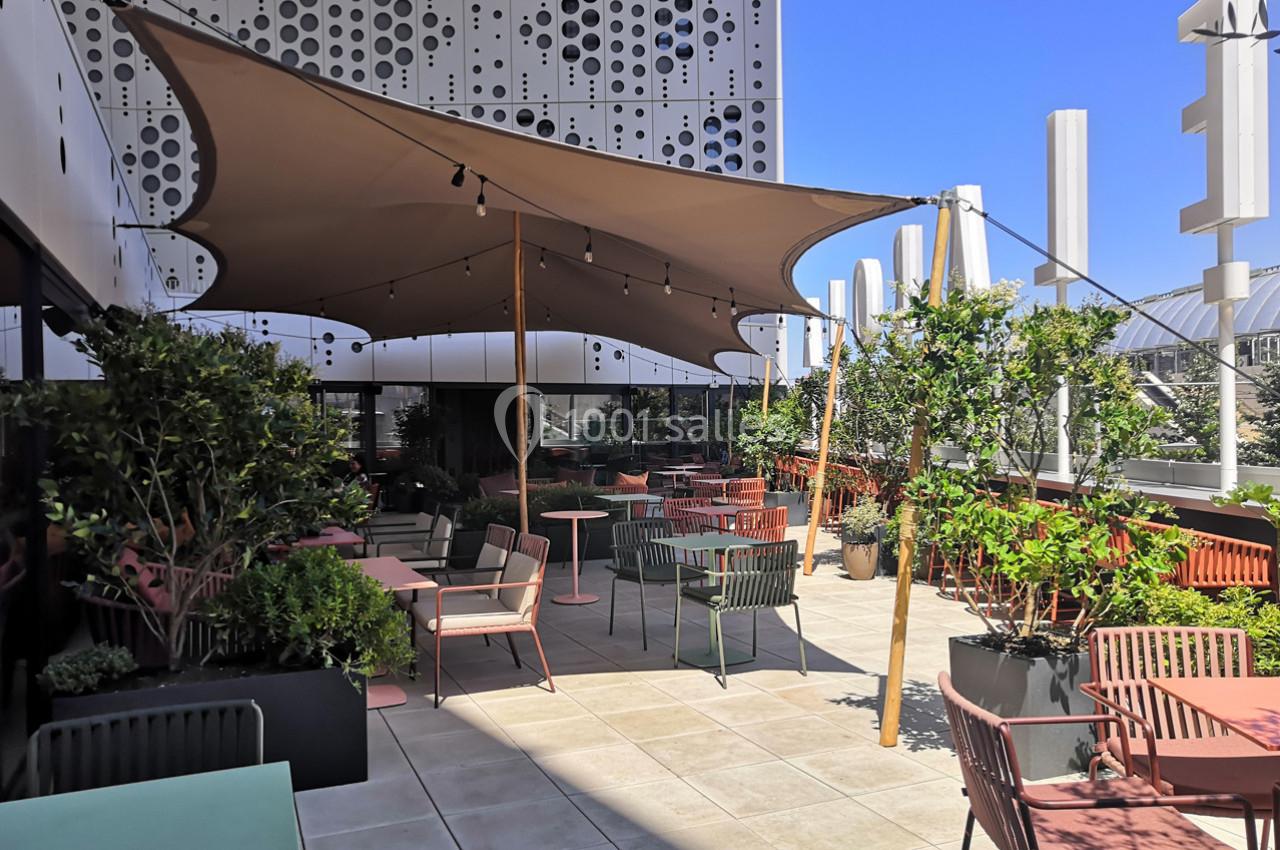 Location salle Montpellier (Hérault) - Hôtel Belaroïa #2 Terrasse aménagée avec des tables, des chaises colorées, des plantes et une toile d'ombrage sous un ciel bleu.