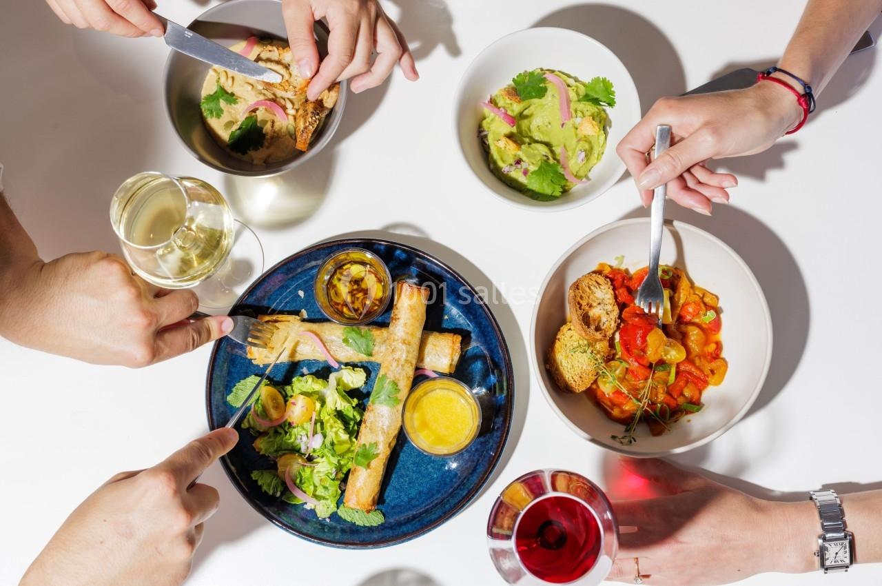 Location salle Montpellier (Hérault) - Hôtel Belaroïa #20 Repas convivial avec plusieurs plats colorés, des mains partageant des assiettes et des verres de vin sur une table blanche.