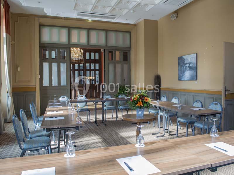 Salle de réunion lumineuse avec tables en bois, chaises bleues, bouquet de fleurs et porte vitrée en arrière-plan.