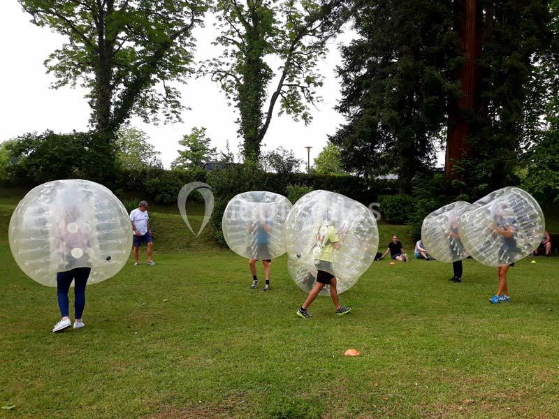 Des personnes jouent au bubble football dans un parc, entourées d'arbres et de pelouse.