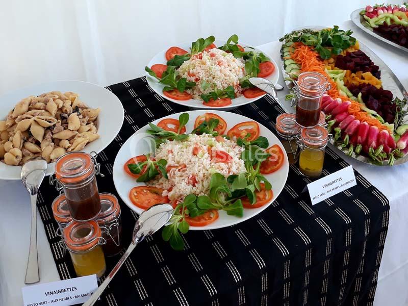 Buffet avec salades composées, légumes frais, champignons, et vinaigrettes variées présentées sur une nappe noire.