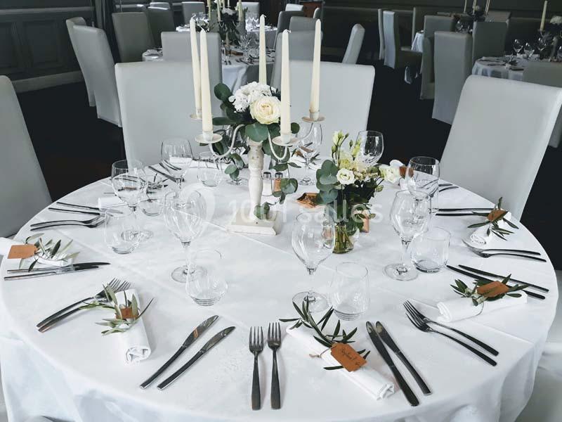 Table ronde élégamment dressée avec nappes blanches, bougies, fleurs et couverts disposés pour un repas formel.