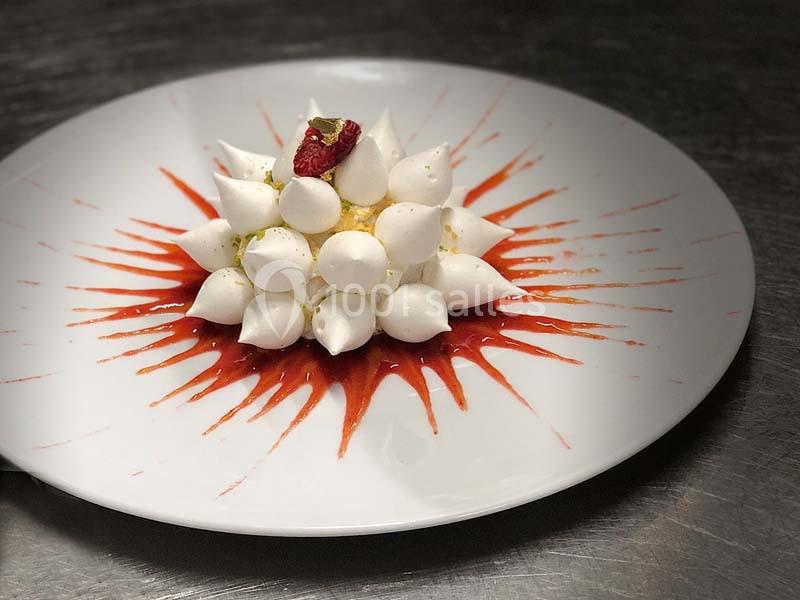 Dessert composé de meringues disposées en dôme sur un coulis rouge, décoré d'une framboise et de feuille d'or.