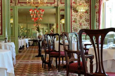 Salle de restaurant élégante avec tables dressées, chaises en bois sculpté et décor floral sur les murs et le sol.
