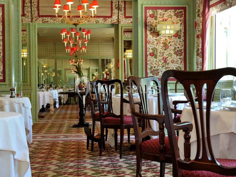 Salle de restaurant élégante avec tables dressées, chaises en bois sculpté et décor floral sur les murs et le sol.
